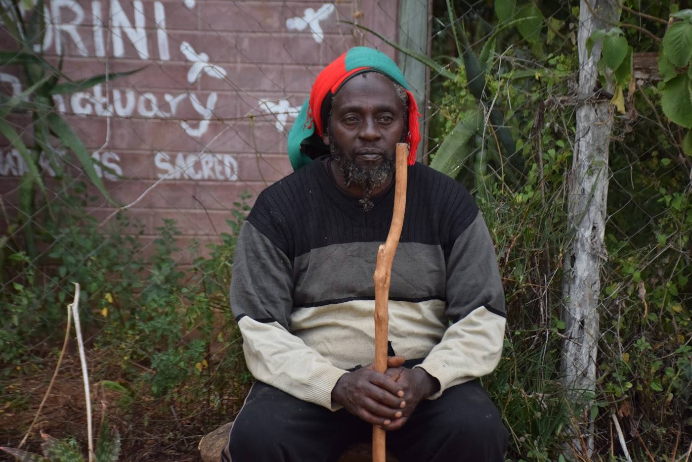 A custodian seated beside a wall painted with the words Porini Sanctuary and 'our lands are sacred'